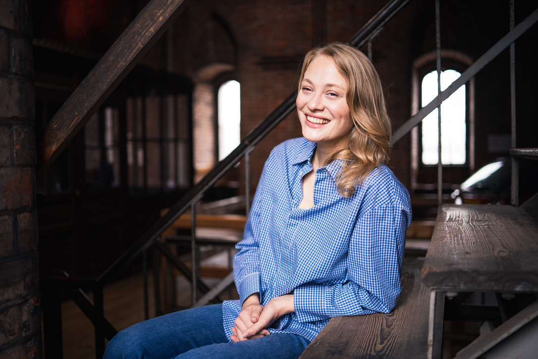 Luca Maya Bartnitzki von Bella Port sitzt lachend auf einer Treppe in einem Backsteinloft