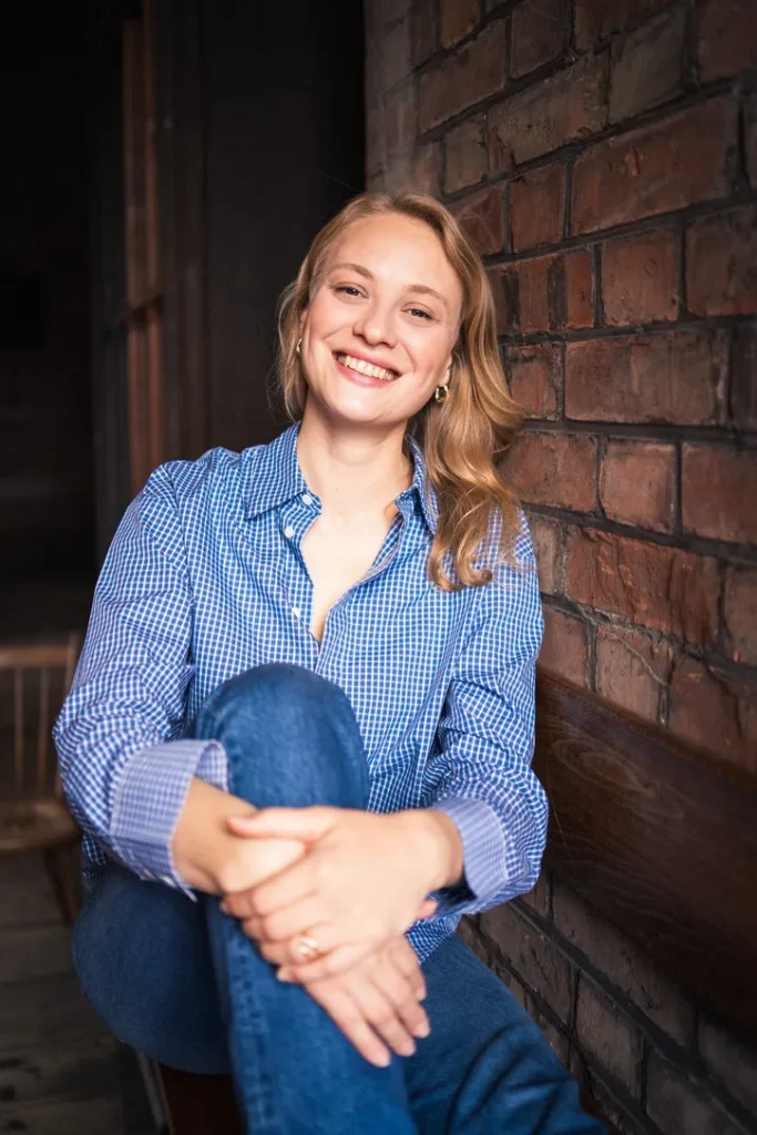 Luca Maya Bartnitzki von Bella Port sitzt lachend vor einer Backsteinwand