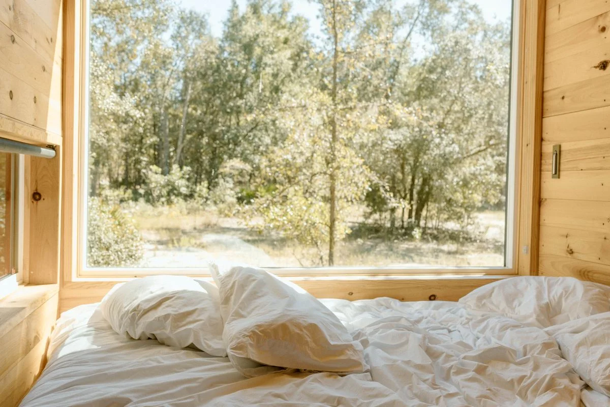 Frau in beigem Hausanzug liest entspannt auf dem Bett in einem ruhigen, minimalistisch eingerichteten Schlafzimmer in warmen Naturtönen